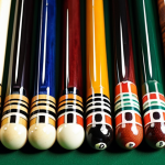**Billiard Cue Stick Selection:** A close-up shot of various billiard cue sticks, highlighting different weights (19-21 ounces) and tip sizes (12-13mm). Focus on a beginner-friendly, medium-weight stick with a stable tip.